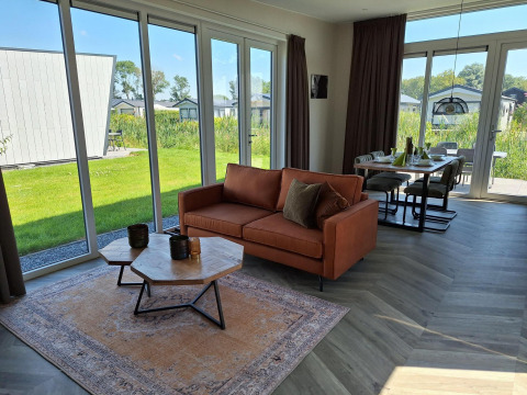 Modern Just Nature lodge at De Rijp, Netherlands, with large windows, sofa, dining area, and outdoor view.
