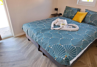 Cama acogedora con ropa de cama verde y toalla en forma de corazón en Just Nature Lodge, De Rijp, Países Bajos.