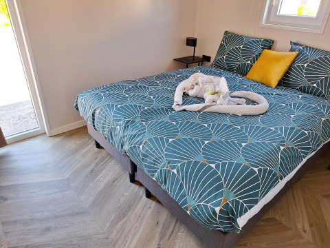 Cozy bed with green patterned bedding and towel heart decor at Just Nature Lodge in De Rijp, Netherlands.