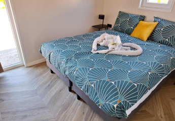 Cama acogedora con ropa de cama verde y toalla en forma de corazón en Just Nature Lodge, De Rijp, Países Bajos.