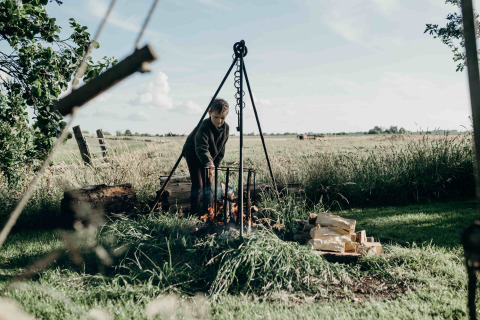 Kind aan kampvuur bij Feather Down TaarTenTuin, vakantiepark in Zuid-Holland, Nederland, zomerse dag.