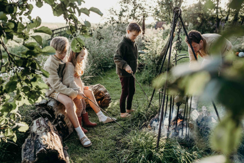 Niños y un adulto disfrutan de una fogata en Feather Down TaarTenTuin, parque vacacional en Sur de Holanda.