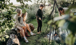 Niños y un adulto disfrutan de una fogata en Feather Down TaarTenTuin, parque vacacional en Sur de Holanda.