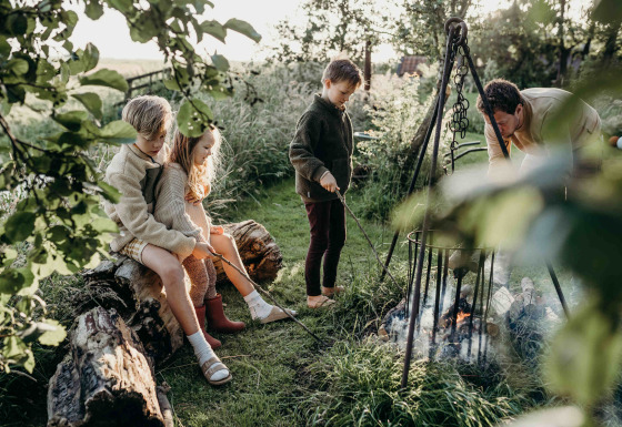 Des enfants et un adulte réunis autour d’un feu de camp à Feather Down TaarTenTuin, Sud-Holland.