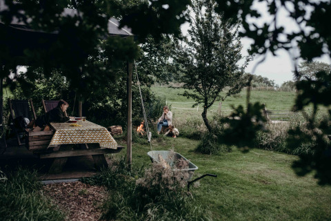Mensen ontspannen aan tafel en bij een kampvuur bij Feather Down TaarTenTuin vakantiepark in Zuid-Holland.