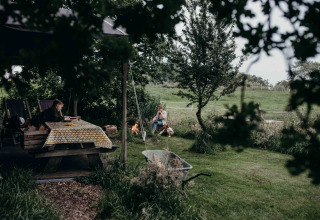 Mensen ontspannen aan tafel en bij een kampvuur bij Feather Down TaarTenTuin vakantiepark in Zuid-Holland.