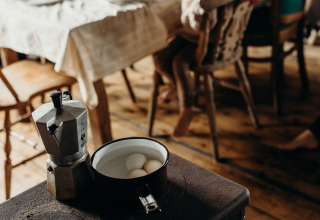 Fornuis met koffiekan en eieren, vage achtergrond met kind aan eettafel in Feather Down TaarTenTuin.