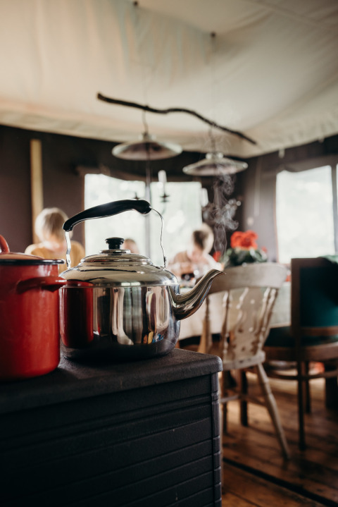 Stomende theeketel op fornuis met familie aan tafel in Feather Down TaarTenTuin vakantiepark.