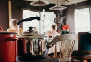 Steaming kettle on the stove with family gathered at table in Feather Down TaarTenTuin holiday park.