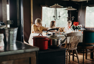 Interieurbeeld bij Feather Down TaarTenTuin, kinderen rond de tafel, gezellige sfeer en houtkachel.