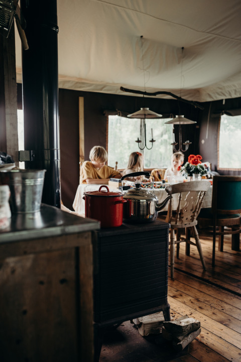 Interieurbeeld bij Feather Down TaarTenTuin, kinderen rond de tafel, gezellige sfeer en houtkachel.