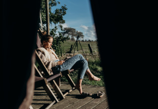 Vrouw leest rustig op een ligstoel op het houten terras, Feather Down TaarTenTuin, Zuid-Holland, Nederland.