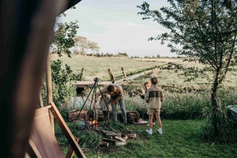 Family enjoys campfire at Feather Down TaarTenTuin holiday park in South Holland, Netherlands, surrounded by nature.