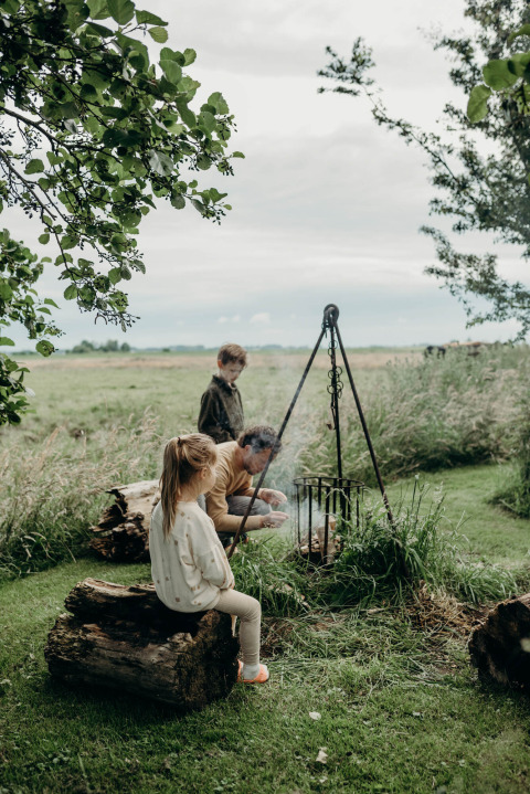 Kinderen en volwassene bij een kampvuur in de natuur bij Feather Down TaarTenTuin, Zuid-Holland.