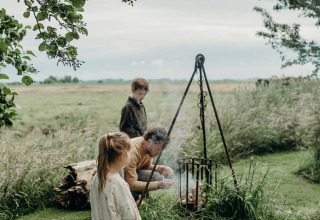 Familie sitzt am Lagerfeuer im Grünen bei Feather Down TaarTenTuin, Südholland, Niederlande.