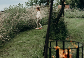 Et barn går i græsset nær et bålsted på Feather Down TaarTenTuin feriepark i Sydholland, Nederlandene.