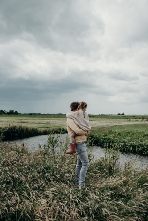 Persoon met kind aan een waterloop in de landelijke omgeving van Aarlanderveen, Zuid-Holland, bewolkt weer.