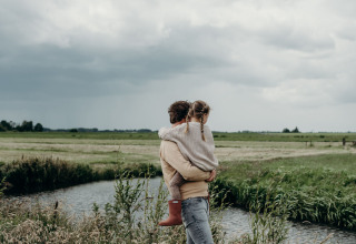 Persoon met kind aan een waterloop in de landelijke omgeving van Aarlanderveen, Zuid-Holland, bewolkt weer.