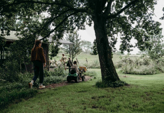 Family exploring Feather Down TaarTenTuin holiday park in South-Holland, Netherlands, beside a large tree.