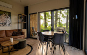 Interior de lodge moderno con sofá de cuero, mesa de comedor, grandes ventanales y vistas al bosque.