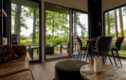 Sala de estar de una cabaña con puertas de cristal al bosque, terraza y comedor moderno con luz natural.