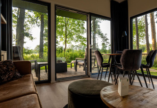 Sala de estar de una cabaña con puertas de cristal al bosque, terraza y comedor moderno con luz natural.