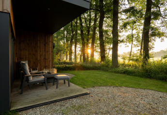 Sonnenaufgang durch Bäume, betrachtet von einer gemütlichen Terrasse an einer Lodge mit Sesseln.
