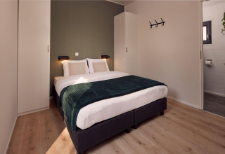 Habitación moderna en una cabaña, cama doble, pared verde, suelo de madera, armarios y baño privado.