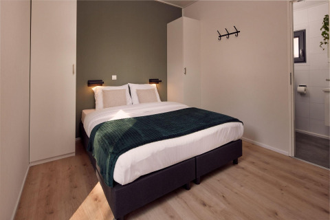 Moderne lodgekamer met dubbel bed, groene accentmuur, houten vloer, kasten en een eigen badkamer.