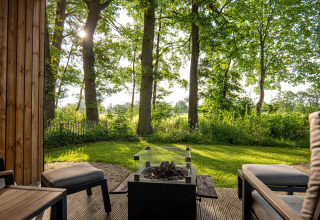 Uitzicht vanaf het terras van een lodge met loungezetels en vuurkorf, omgeven door groene natuur.