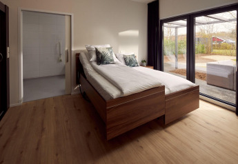 Wheelchair-friendly bedroom with wooden floor, twin beds, and large windows facing patio in the Netherlands.