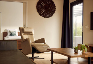 Salón de Holiday villa Amalia 2 en Hofparken Wiltershaar, Países Bajos, con sillón y mesa de madera.