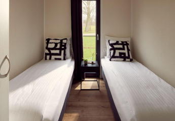 Dos camas individuales y una pequeña mesa en una habitación luminosa de Holiday villa Amalia 6, Hofparken Wiltershaar, Países Bajos.