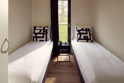 Dos camas individuales y una pequeña mesa en una habitación luminosa de Holiday villa Amalia 6, Hofparken Wiltershaar, Países Bajos.