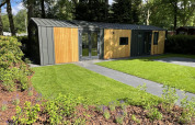 Et moderne Cozy Chalet-lodge ved Veluwepark de Bosgraaf i Holland, omgivet af grønt græs og træer.