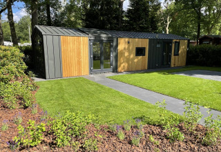 Een modern Cozy Chalet in Veluwepark de Bosgraaf in Nederland, omringd door gras en groene bomen.