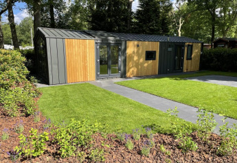 Et moderne Cozy Chalet-lodge ved Veluwepark de Bosgraaf i Holland, omgivet af grønt græs og træer.