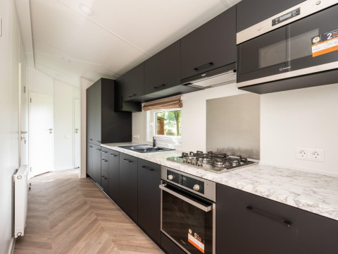 Cocina moderna negra con encimera de mármol en Cozy Chalet en Veluwepark de Bosgraaf, Países Bajos.