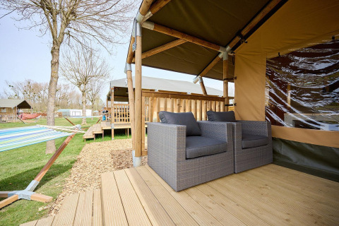 Terraza de tienda safari con sillones y hamaca en Camping 't Geuldal, Países Bajos.