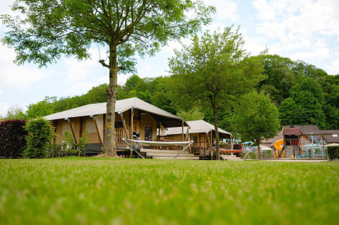 Safaritent Villatent Cottage op Camping 't Geuldal in Nederland, omgeven door grasvelden en bomen.