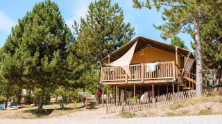 Villatent Nomad Lodge auf Camping La Presqu’île in Frankreich, umgeben von Pinien, auf Holzplattform.