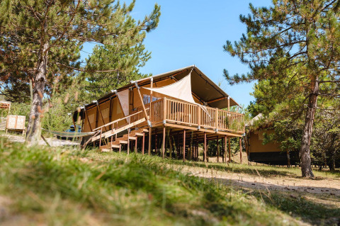 Tienda de lujo Villatent Nomad sobre una terraza de madera en Camping La Presqu’île, Francia, rodeada de árboles.