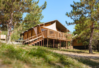 Tienda de lujo Villatent Nomad sobre una terraza de madera en Camping La Presqu’île, Francia, rodeada de árboles.