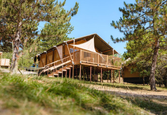 Tienda de lujo Villatent Nomad sobre una terraza de madera en Camping La Presqu’île, Francia, rodeada de árboles.