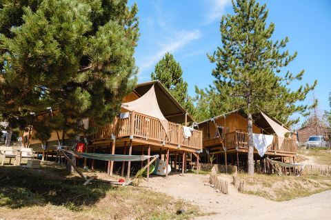 Tiendas tipo safari en Villatent Nomad, Camping La Presqu’île, Francia, rodeadas de pinos y hamacas.