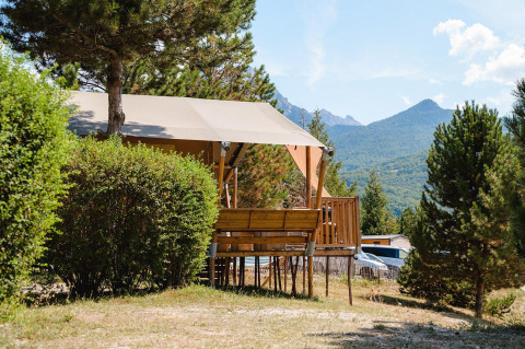 Villatent Nomad lodge al Camping La Presqu’île in Francia, circondata da alberi e montagne sullo sfondo.