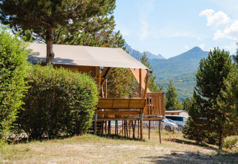 Villatent Nomad lodge al Camping La Presqu’île in Francia, circondata da alberi e montagne sullo sfondo.