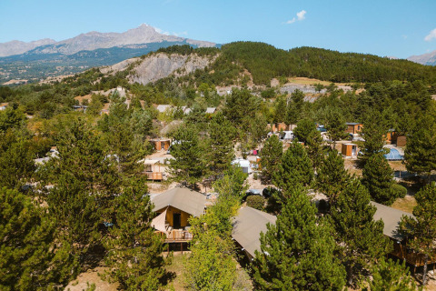 Vista aérea de la lodges Villatent Nomad en Camping La Presqu’île, Francia, rodeadas de árboles y montañas.