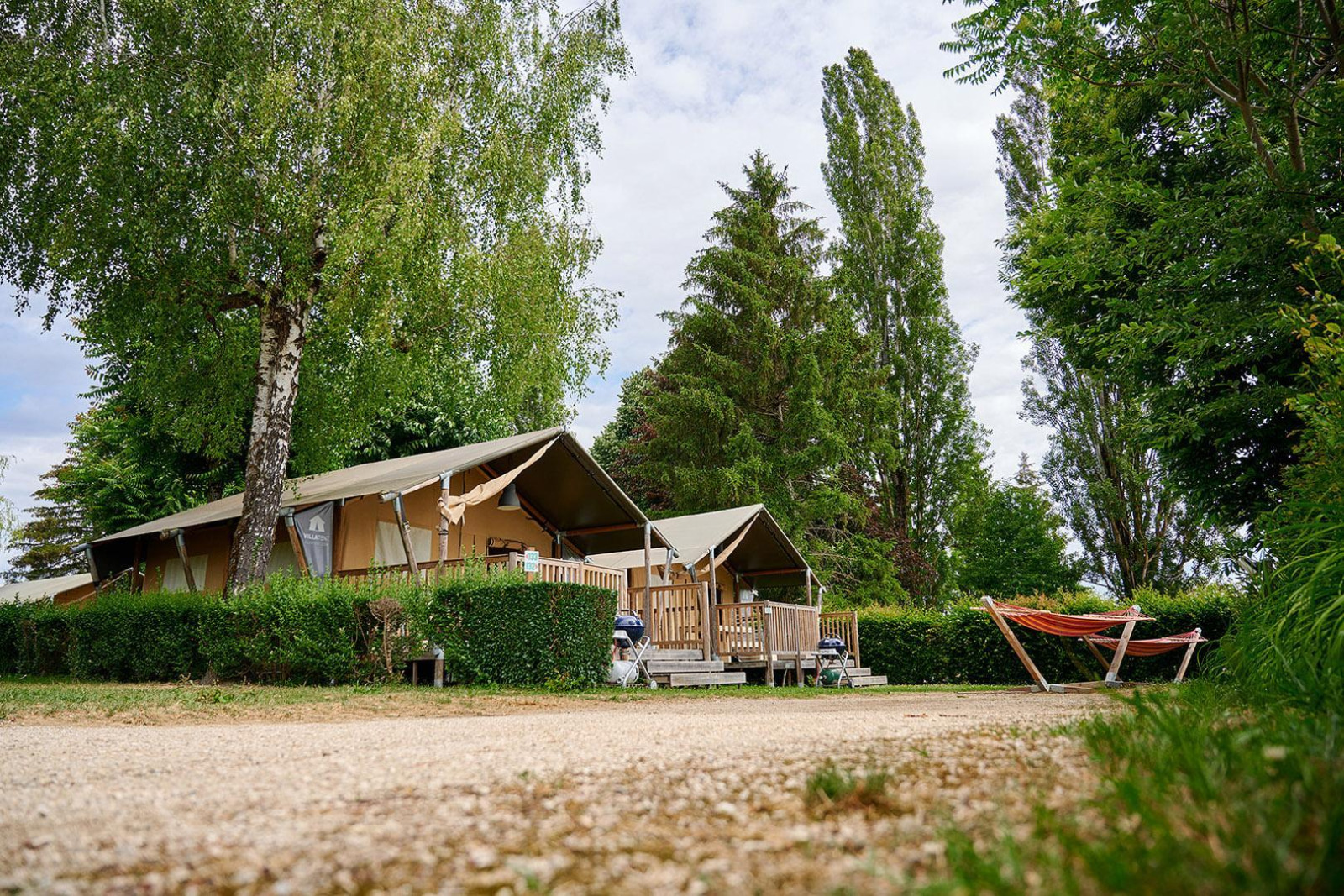 Safaritent Villatent Wood op Camping Le Coin Tranquille in Frankrijk, omringd door bomen en een oranje hangmat.