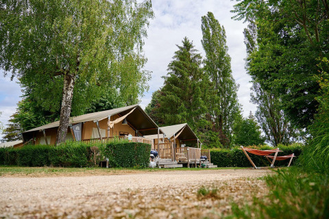 Safaritent Villatent Wood op Camping Le Coin Tranquille in Frankrijk, omringd door bomen en een oranje hangmat.